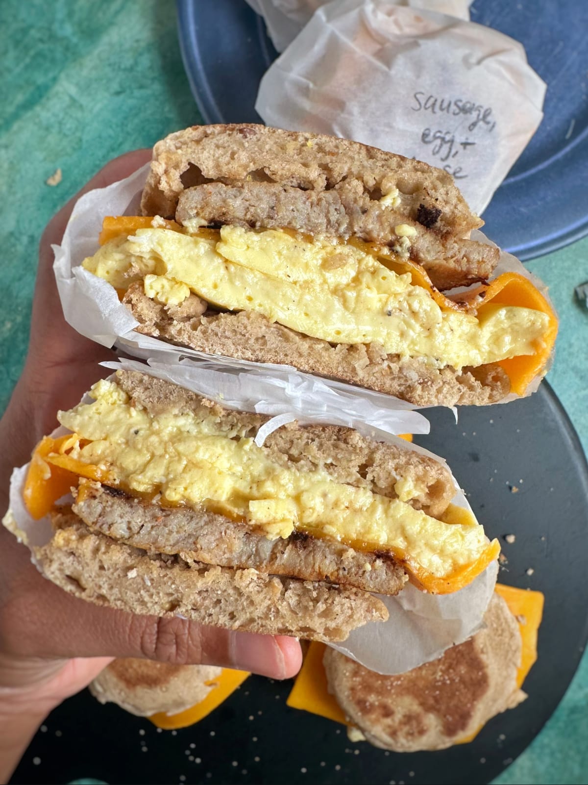 A sausage breakfast sandwich cut to see the cross section with more sandwiches assembled in the background.