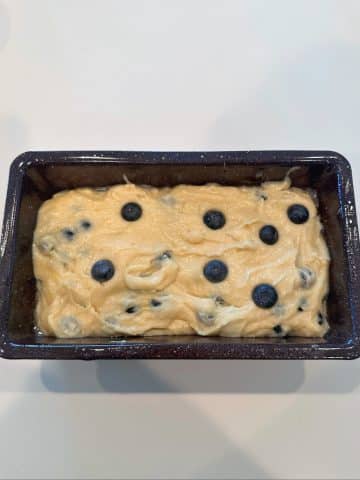 A loaf pan filled with cake batter and fresh blueberries.