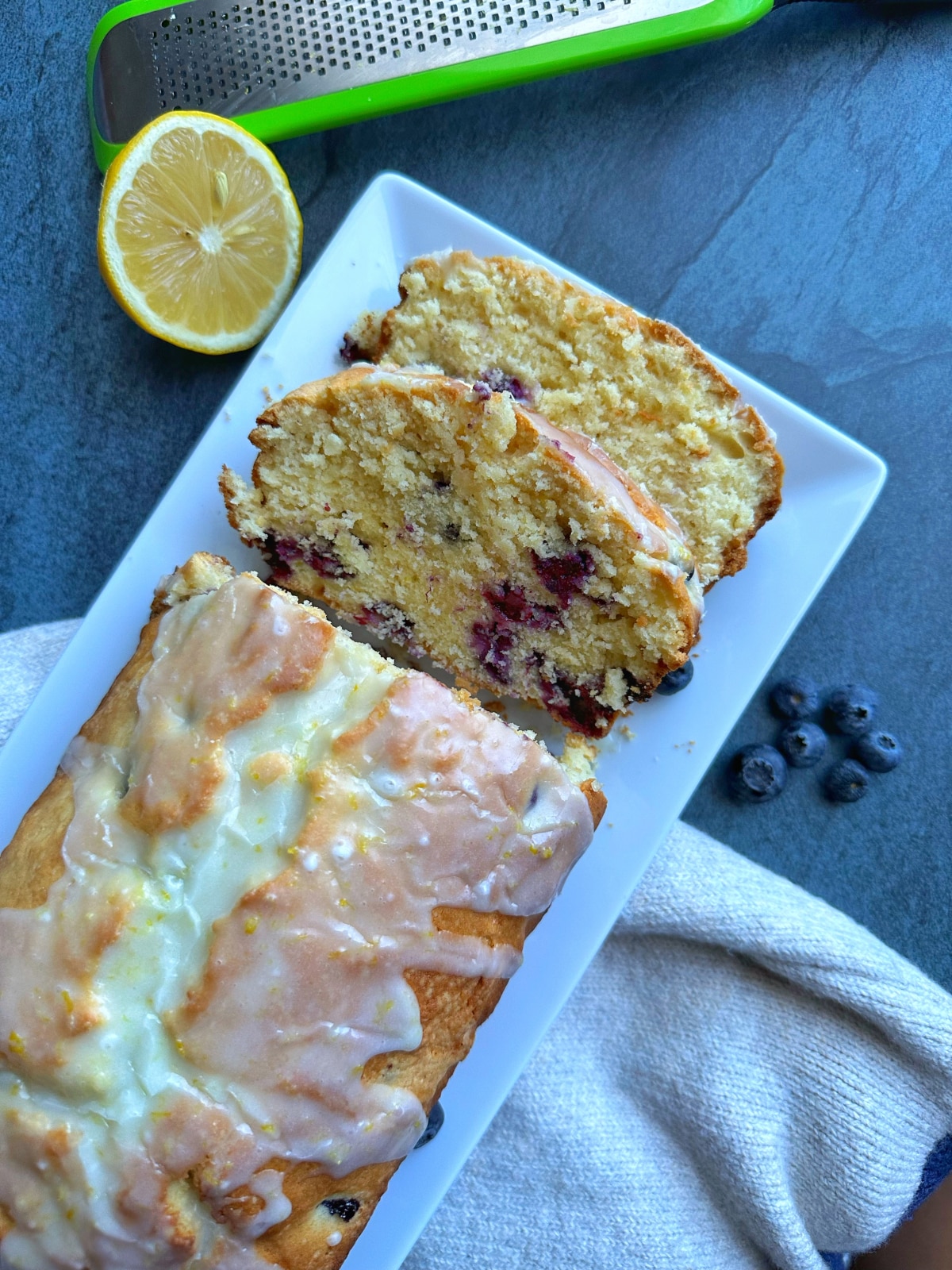 A loaf of lemon blueberry cake with a couple slices cut out of it, and lemon slices on the side.