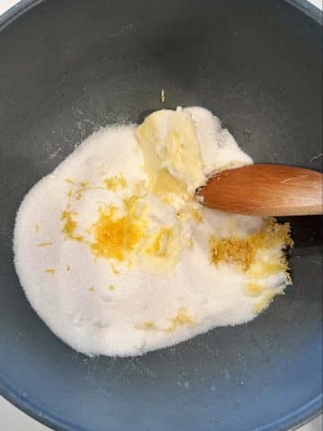 A wooden spoon mixing together sugar, lemon zest, and softened butter.
