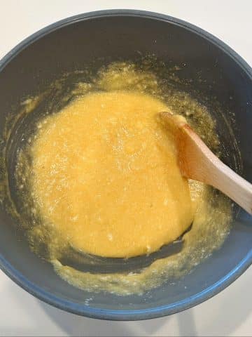 A mixing bowl with a wooden spoon stirring a yellow batter.