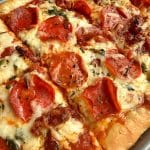 A tray of personal pan pizza with turkey pepperoni, sun-dried tomatoes, and spinach.