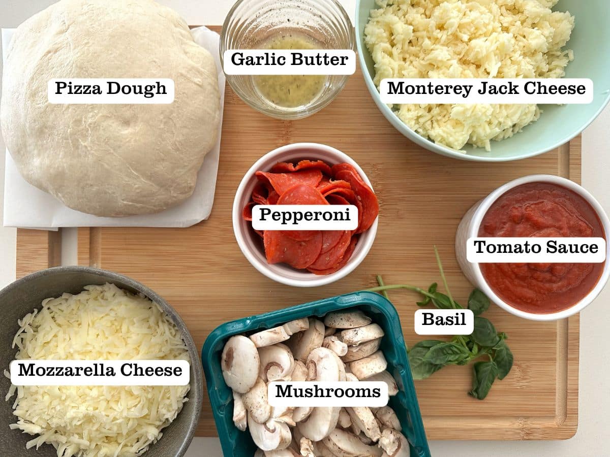 A wooden board containing ingredients for pan pizza - including dough, cheese, and fresh basil.