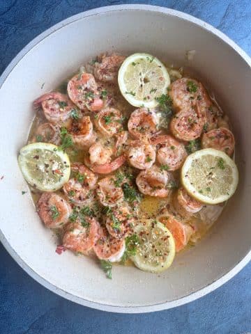 A pan of shrimp scampi with lemon slices and chopped parsley.
