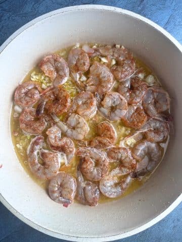 A pan of raw shrimp, cooking in a butter wine sauce.