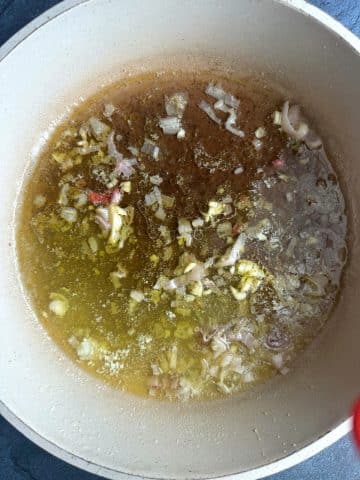 A pan of sautéed shallot, garlic, and butter with white wine inside.