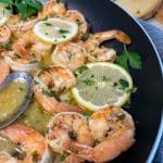 Skillet with garlic butter shrimp scampi, lemon slices, and parsley with bread on the side.