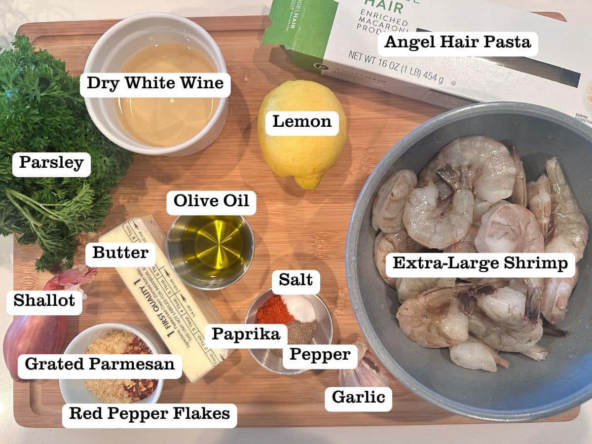 A wooden board containing ingredients for Shrimp Scampi, including butter, white wine, shrimp and pasta.