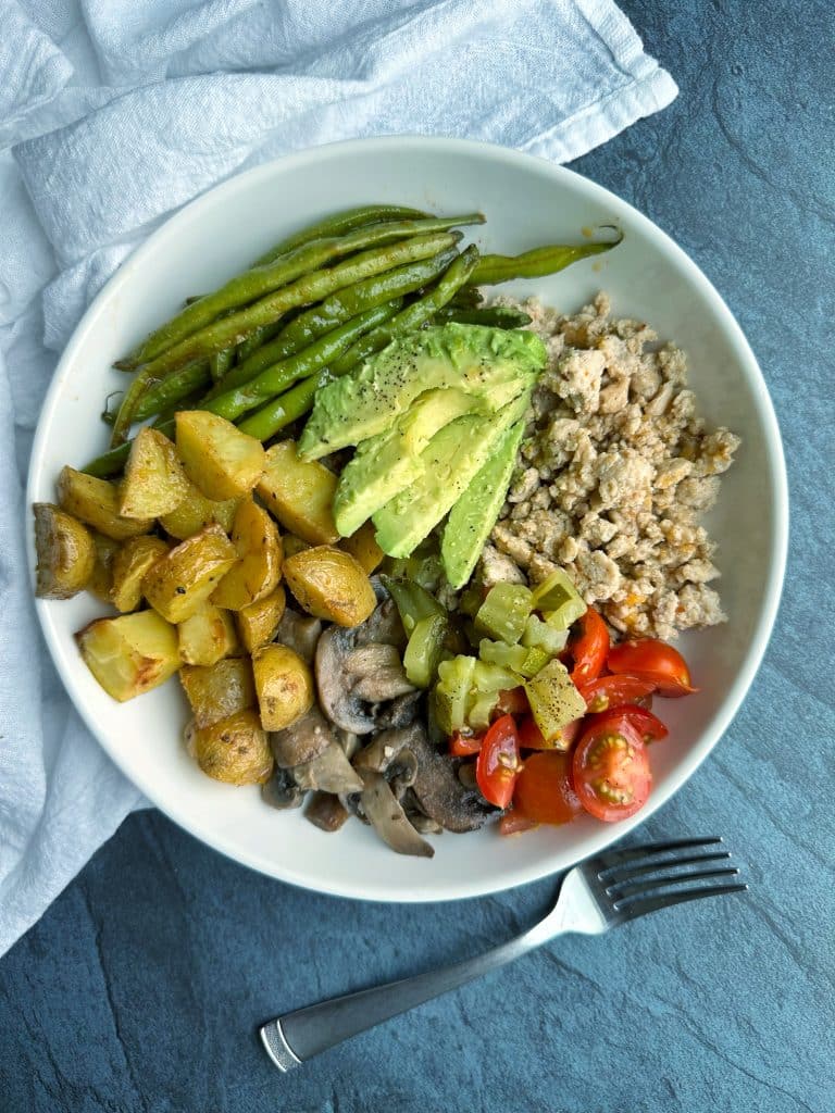 A Ground Chicken Burger Bowl with chicken, tomatoes, pickles, roasted potatoes, green beans, and avocado.