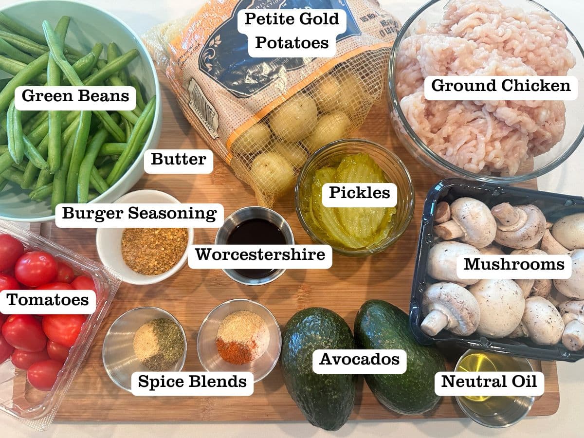 A wooden board containing ingredients for burger bowls, including ground chicken, green beans, potatoes, and avocados. 