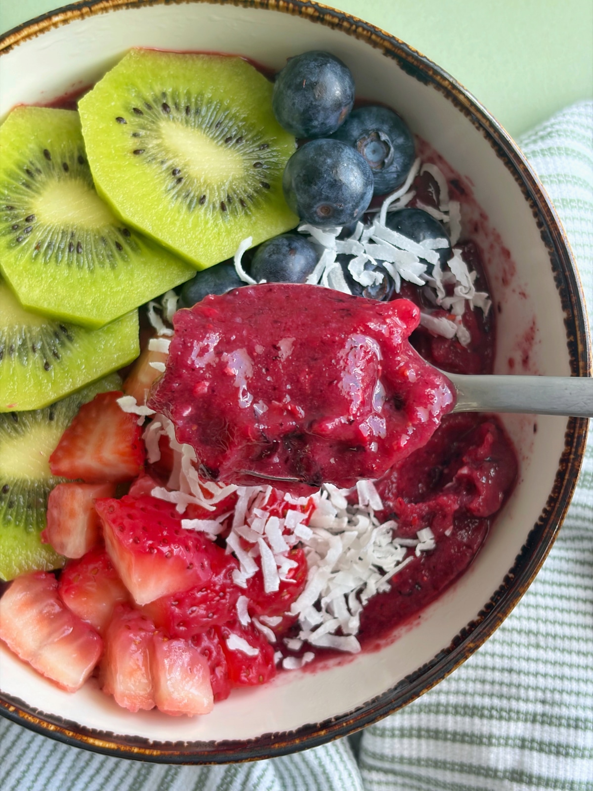 A spoon displaying a bite of a mixed berry smoothie bowl, over the rest of the dish.