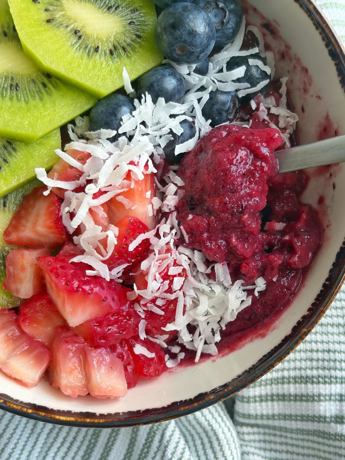 A closeup shot of a mixed berry smoothie bowl with a spoon sticking out of it.
