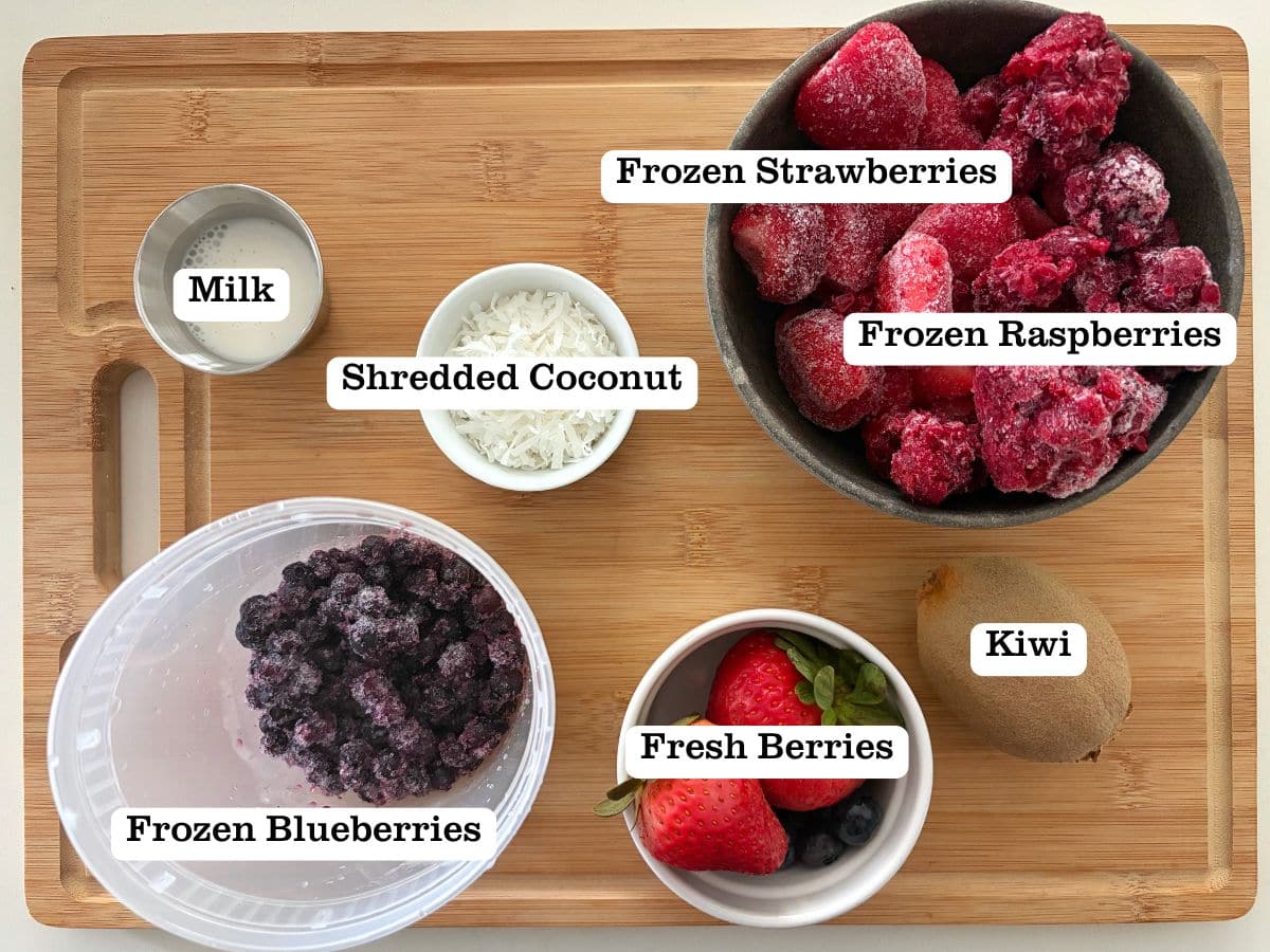 A wooden bowl with containers of ingredients for a berry smoothie bowl.