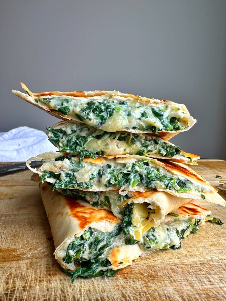 A stack of four Spinach Dip Quesadillas on a wooden board.