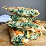 A stack of four Spinach Dip Quesadillas on a wooden board.