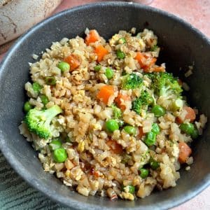 A bowl of cauliflower fried rice with carrots, peas, and broccoli.