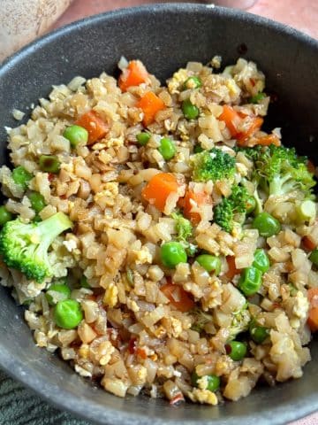 A bowl of cauliflower fried rice with carrots, peas, and broccoli.
