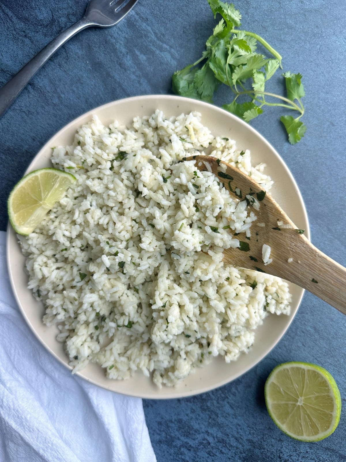 Rice with lime and cilantro on a plate with a wooden spoon sticking out of it.