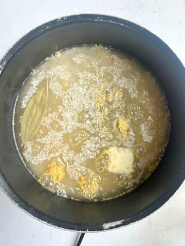 A pot filled with water, yellow seasoning, butter, and rice.
