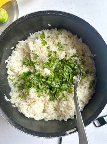 A pot of fluffy cooked rice with chopped cilantro and a spoon sticking out of it.