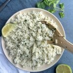 A plate of homemade cilantro-lime rice with a wooden spoon sticking inside.