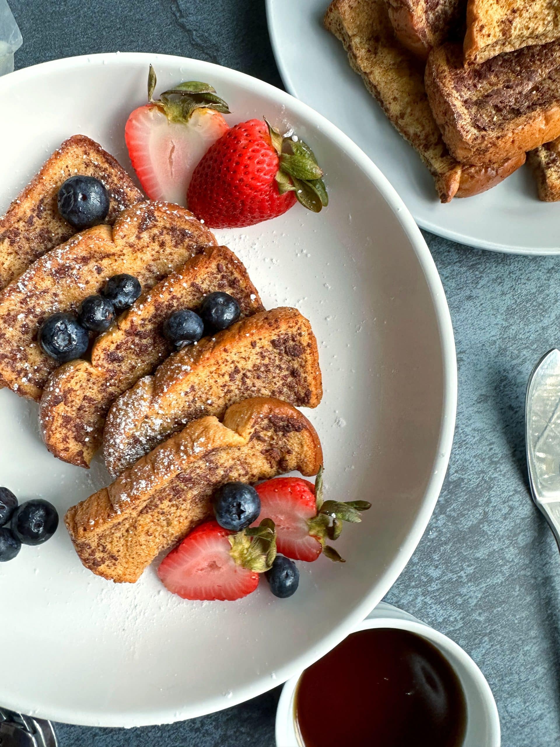 A plate of baked French toast sticks with berries and powdered sugar.