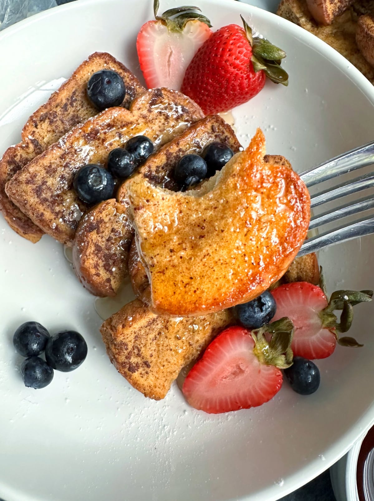 A fork picking up a bite of a baked French toast stick, with more French toast sticks in the background.