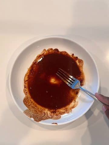 A shallow bowl with a brown liquid of whisked cinnamon and vanilla extract.