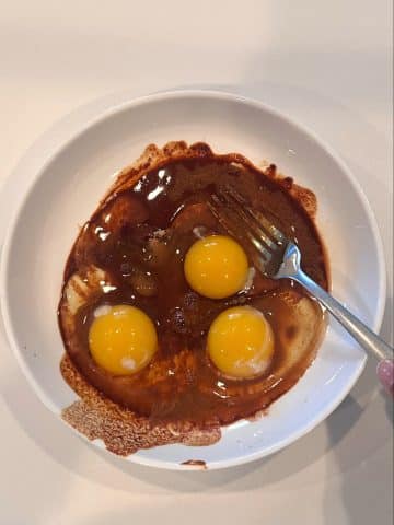 A bowl filled with eggs on top of a brown dipping liquid for French toast.
