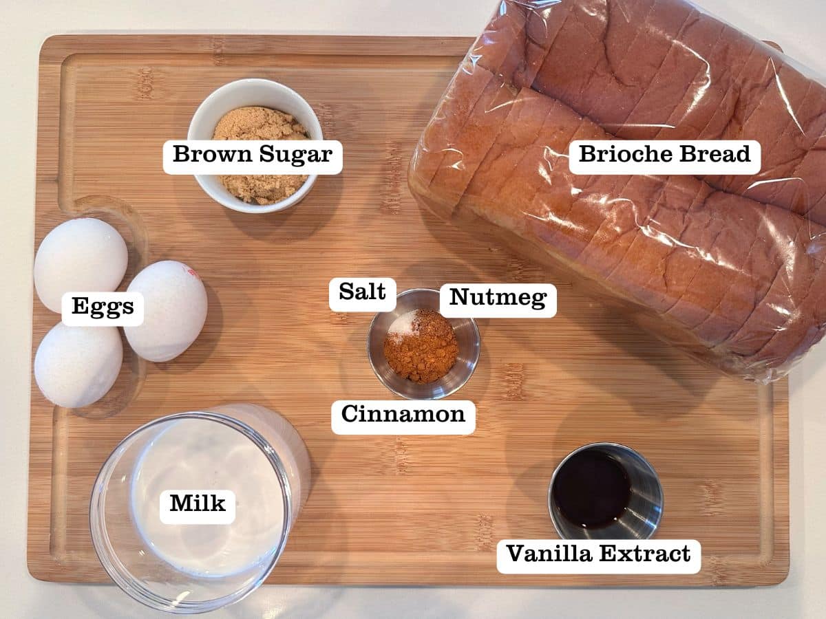 A wooden board containing ingredients for baked French toast sticks, including bread, milk, eggs, and brown sugar.