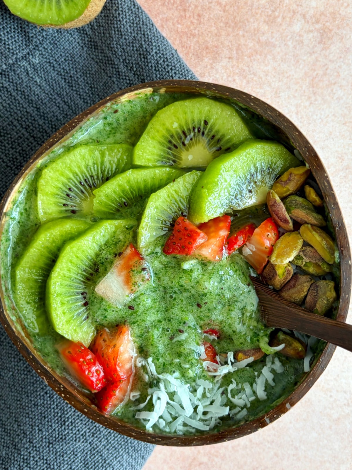 A spoon scooping up a portion of green smoothie out of a brown bowl.