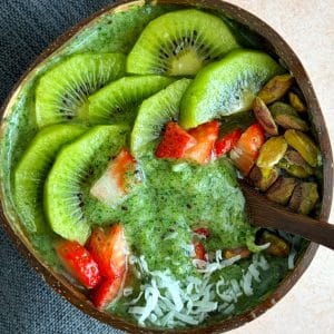 A green smoothie bowl with sliced kiwi, strawberries, and pistachios as toppings.