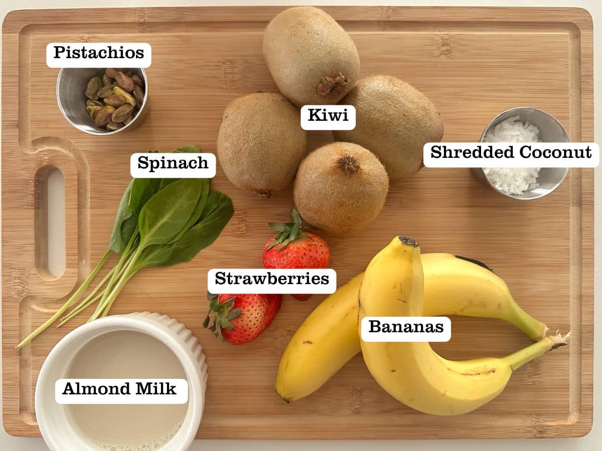 A wooden board containing ingredients for a green smoothie bowl, including kiwis and spinach.