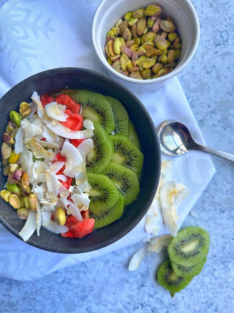 A Green Smoothie Bowl topped with kiwi, strawberries, shredded coconut, and pistachios.