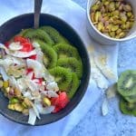 A Green Smoothie Bowl topped with kiwi, strawberries, shredded coconut, and pistachios.