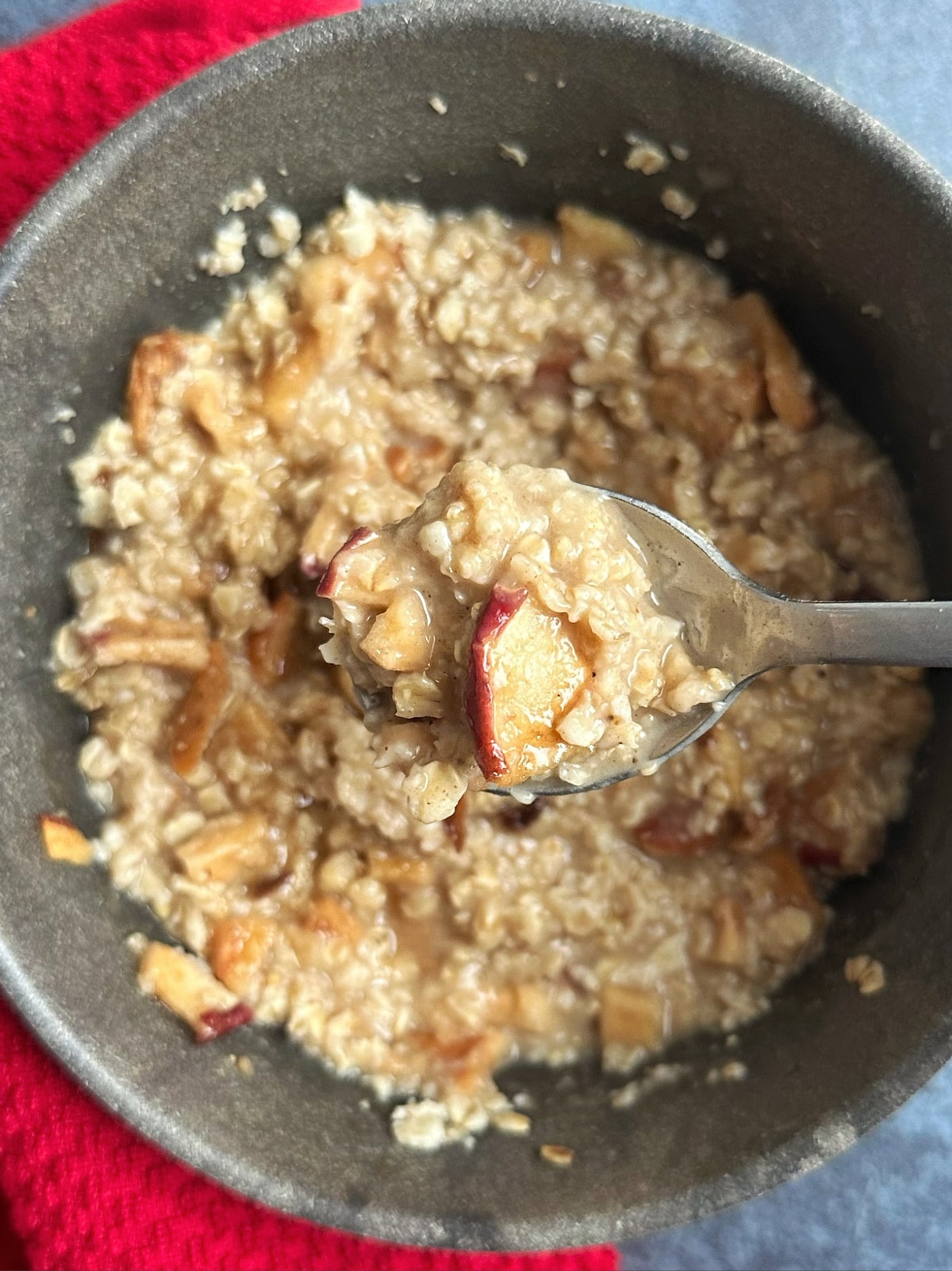 A bowl of apple pie oatmeal, with a spoonful being displayed over the bowl.
