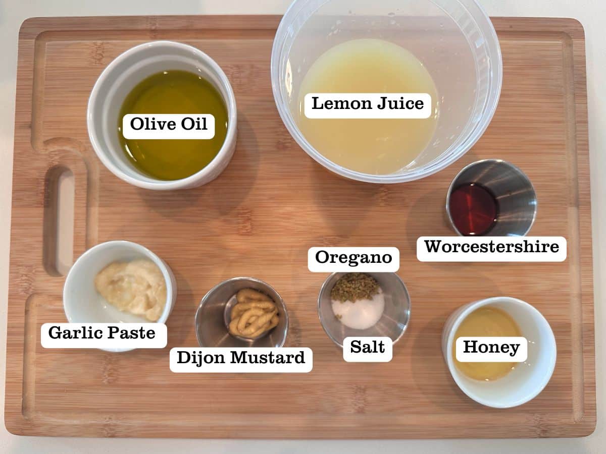 A wooden board containing ingredients for a lemon herb vinaigrette salad dressing.