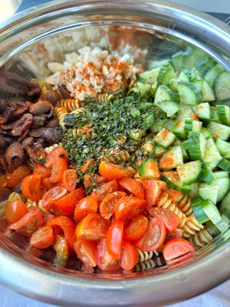 A bowl with all the ingredients for High-Protein Mediterranean Pasta Salad.
