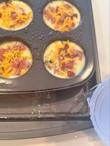 Water being poured into a sheet pan with a filled muffin pan on top.
