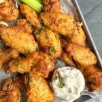 A tray of crispy oven-baked chicken wings with a cup of homemade ranch and celery sticks.