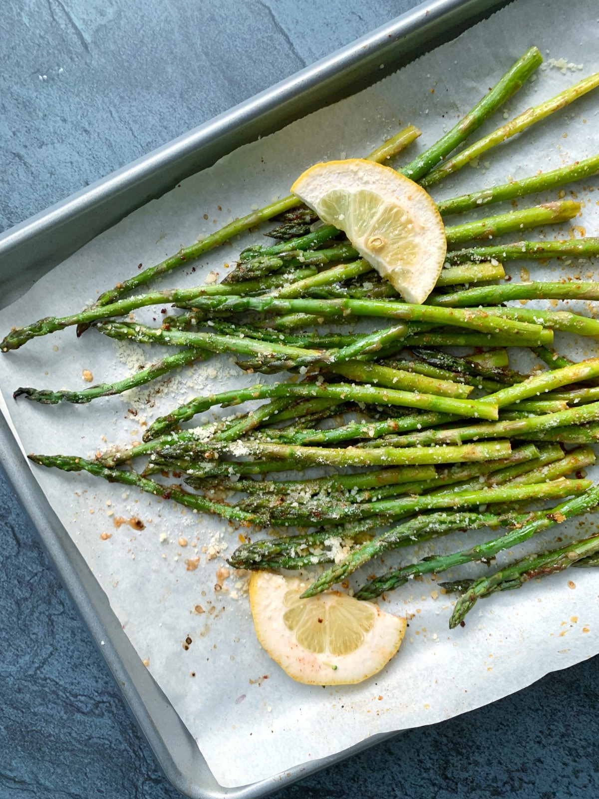 A large pan of roasted asparagus with parmesan and lemon slices.