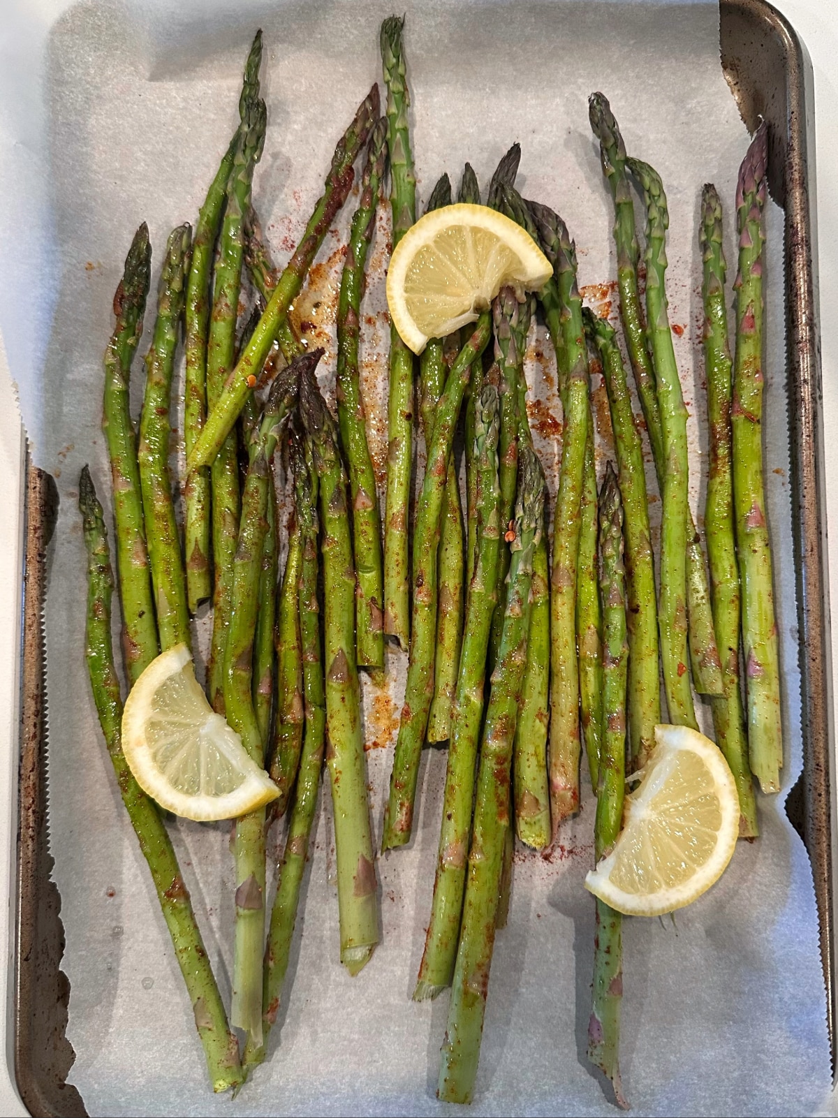 Seasoned asparagus on a sheet pan with lemon slices, ready to be roasted.