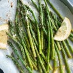 A pan of sheet-pan roasted asparagus with lemon slices and grated parmesan on top.
