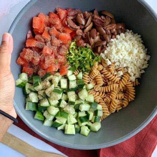 Ingredients for high-protein Mediterranean/Greek Pasta Salad in a large bowl.