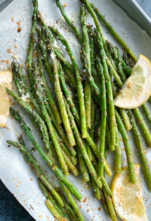 A pan of sheet-pan roasted asparagus with lemon slices and grated parmesan on top.