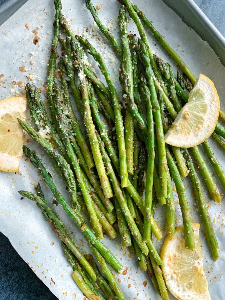 A pan of sheet-pan roasted asparagus with lemon slices and grated parmesan on top.