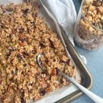 A sheet pan full of homemade chunky granola with a spoon inside.