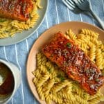 Two plates of Honey Soy Salmon over creamy pasta with more honey soy sauce on the side.