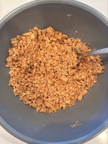 A mixing bowl containing crushed graham crackers and coconut oil combined.