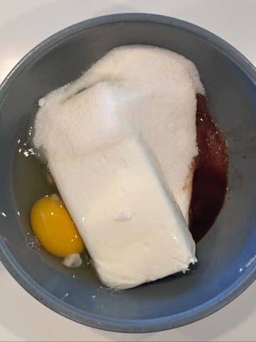 A mixing bowl containing cream cheese, eggs, sugar, and vanilla extract.